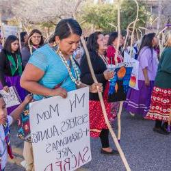 Woman holding sign, "My mom, sisters, aunties + grandmas are sacred'